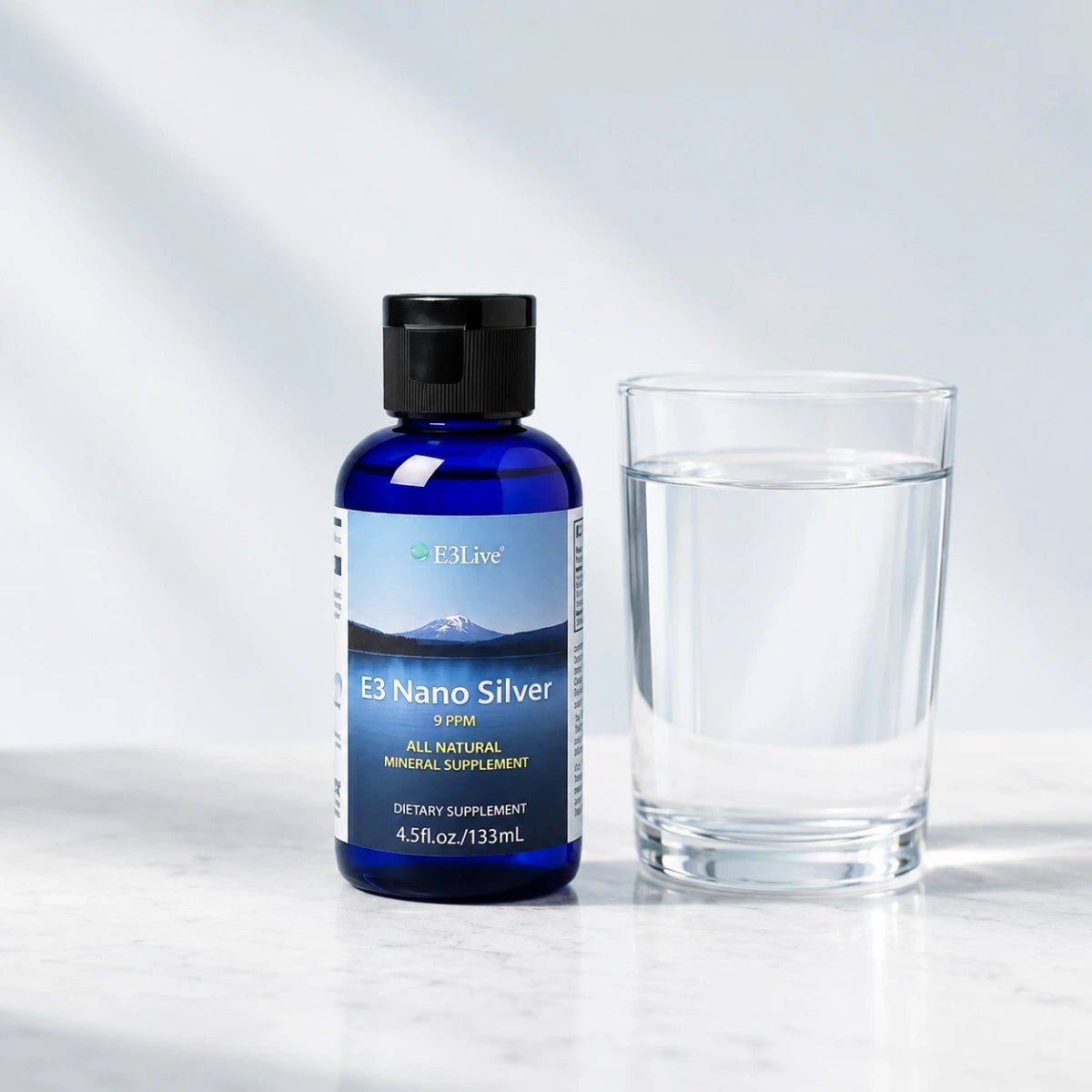 
                  
                    E3 Nano Silver 9 ppm 133 mL bottle standing on marble beside a clear glass of water
                  
                