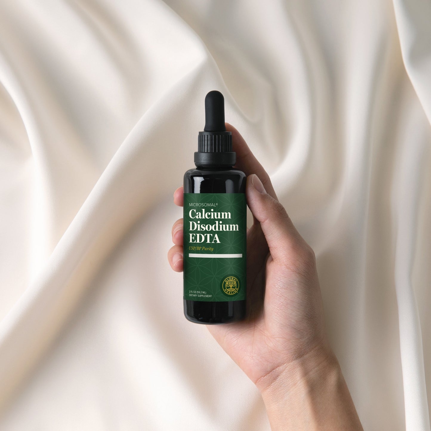 
                  
                    Hand holding the Global Healing Calcium Disodium EDTA 59.2ml bottle against cream silk
                  
                