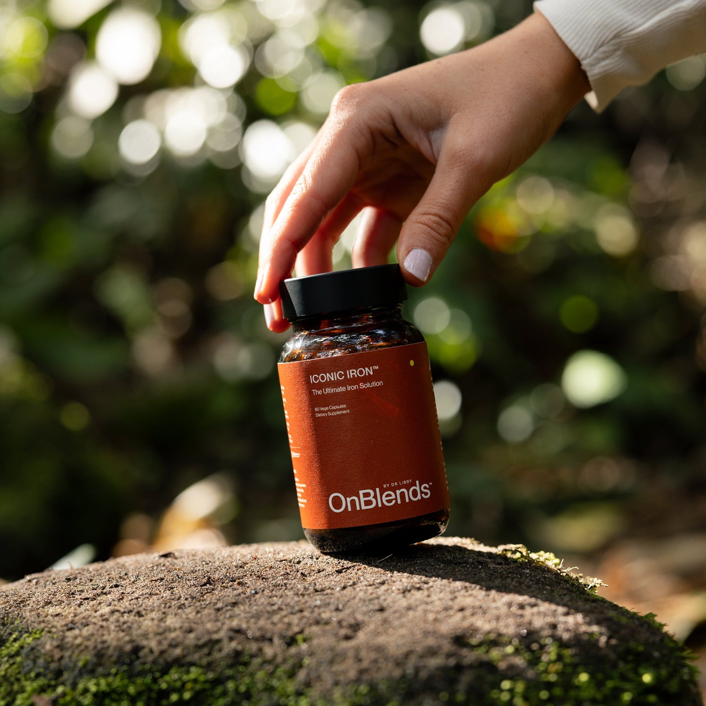 
                  
                    Hand placing the OnBlends Iconic Iron bottle on a mossy rock outdoors
                  
                