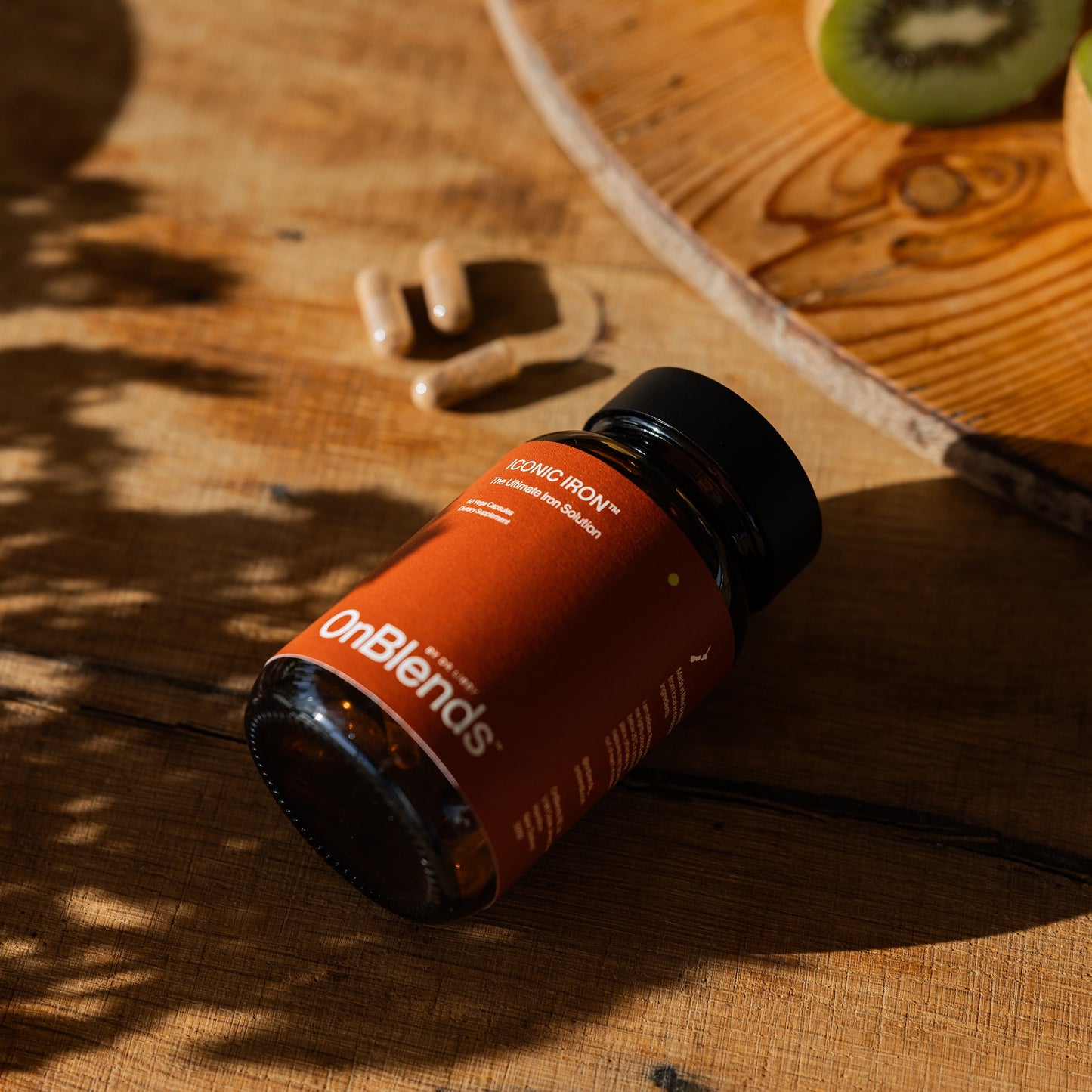 
                  
                    OnBlends Iconic Iron bottle lying on a timber board with vege capsules and kiwifruit
                  
                