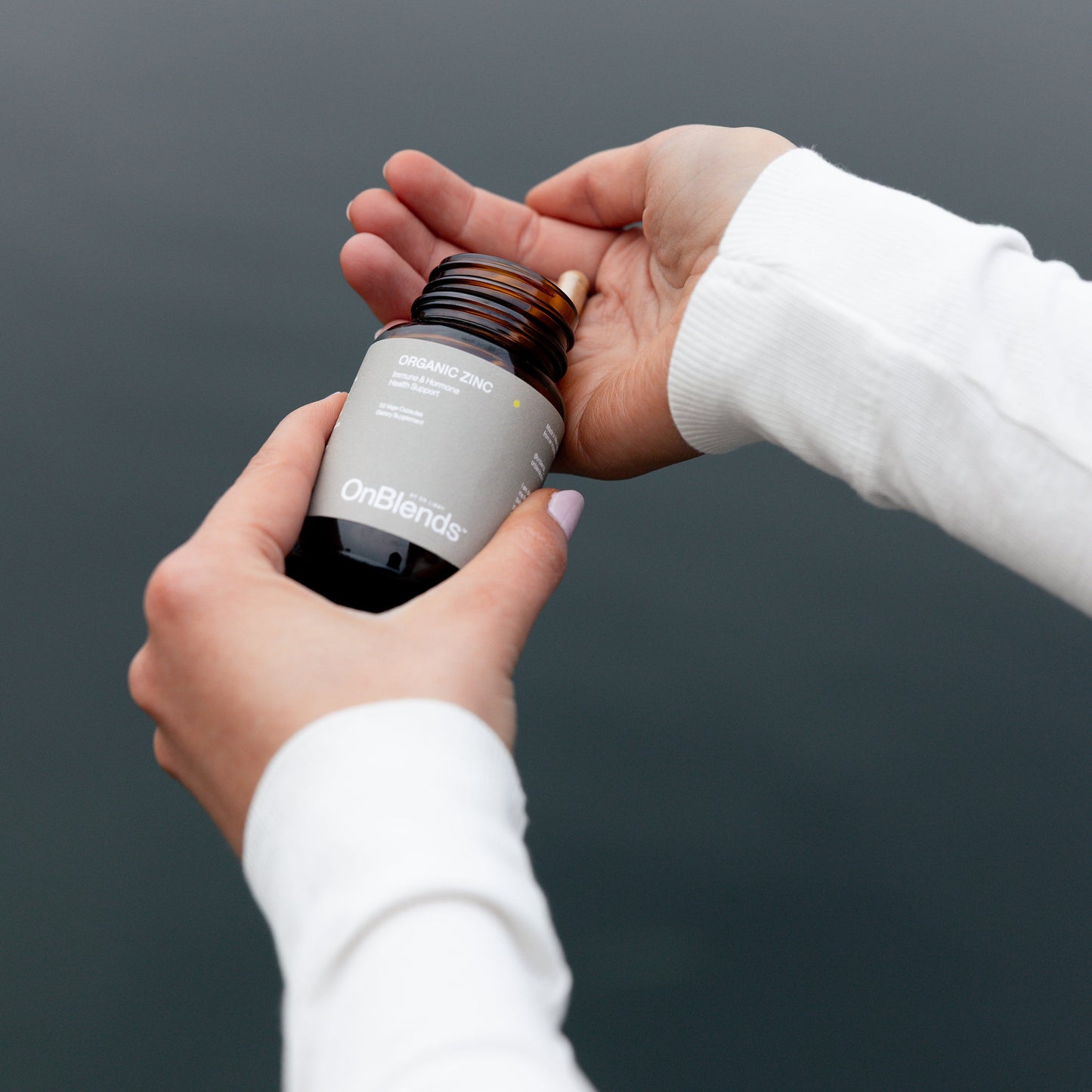 
                  
                    Hands opening the OnBlends Organic Zinc bottle against a dark grey background
                  
                